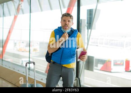 voyage de vacances et tourisme pendant le covid19 - jeune homme attrayant énervé et fatigué de porter un masque facial aux départs de l'aéroport salon avec passeport Banque D'Images