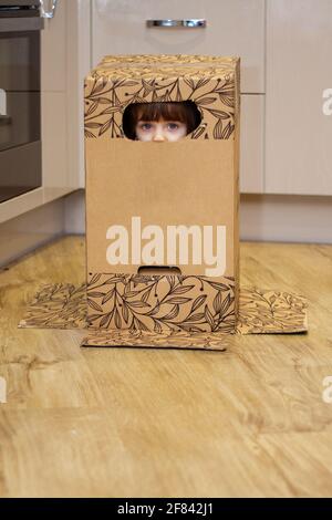 Portrait d'une jolie petite fille à yeux bleus jouant avec une boîte en carton et se cachant à l'intérieur Banque D'Images