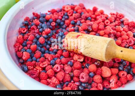 Framboises et groseilles à maquereau dans un bol avec un poussoir, faisant de la confiture maison Banque D'Images