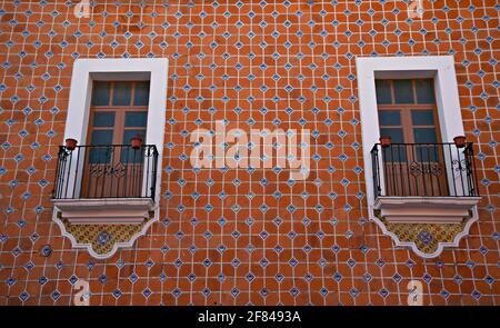 Façade de maison coloniale avec un mur recouvert de carreaux Talavera, bordure blanche autour des fenêtres et balustrades de balcon en fer artisanal à Cholula, Puebla Mexique. Banque D'Images