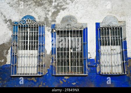 Les fenêtres de la maison coloniale vent des grilles de fer artisanales sur un mur de stuc bleu et blanc délavé à Cholula, Puebla Mexique. Banque D'Images