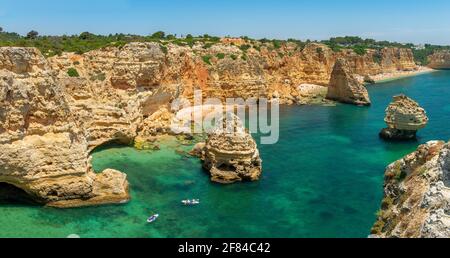 Vue sur la falaise de rochers de grès escarpé, formations rocheuses et kayakistes dans la mer turquoise, plage de sable, Praia da Marinha, Algarve, Lagos, Portugal Banque D'Images