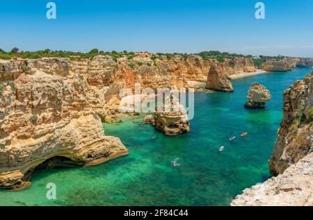 Vue sur la falaise de rochers de grès escarpé, formations rocheuses et kayakistes dans la mer turquoise, plage de sable sur la falaise, Praia da Marinha, Algarve Banque D'Images