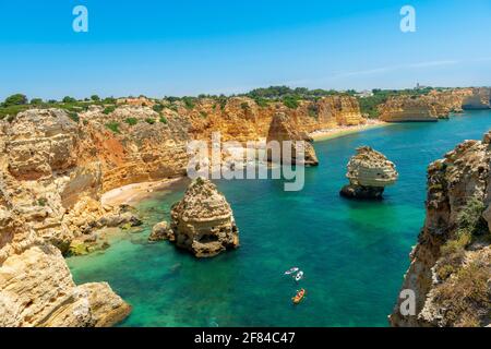 Vue sur la falaise de rochers de grès escarpé, formations rocheuses et kayakistes dans la mer turquoise, plage de sable sur la falaise, Praia da Marinha, Algarve Banque D'Images