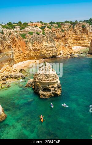 Vue sur la falaise de rochers de grès escarpé, formations rocheuses et kayakistes dans la mer turquoise, plage de sable sur la falaise, Praia da Marinha, Algarve Banque D'Images