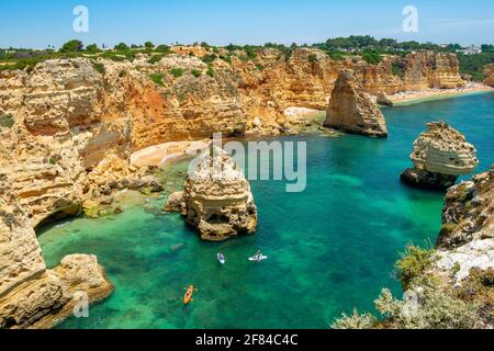 Vue sur la falaise de rochers de grès escarpé, formations rocheuses et kayakistes dans la mer turquoise, plage de sable sur la falaise, Praia da Marinha, Algarve Banque D'Images