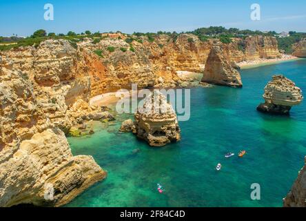 Vue sur la falaise de rochers de grès escarpé, formations rocheuses et kayakistes dans la mer turquoise, plage de sable sur la falaise, Praia da Marinha, Algarve Banque D'Images