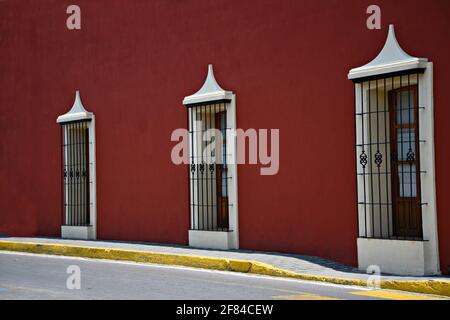 Façade de maison coloniale avec un mur en stuc rouge vénitien, bordure blanche autour des fenêtres et grilles en fer artisanales à Cholula, Puebla Mexique. Banque D'Images