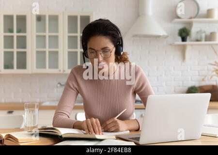 Une jeune femme réfléchie travaille par ordinateur dans la littérature d'étude sur les micro-casques/oreillettes Banque D'Images