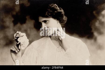 Carte postale photographique d'archives d'une jeune femme tenant une fleur, c. 1910. Banque D'Images