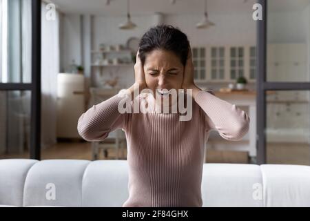 Frustrée femme hispanique millénaire devenir folle écouter le bruit dérangeant à l'intérieur Banque D'Images