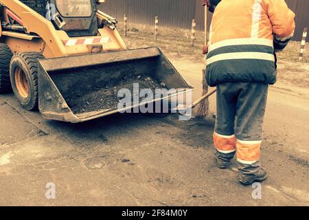 Les travailleurs de la route en uniforme réfléchissant orange vif utilisent des pelles pour gratter le sable accumulé. Entretien des chaussées et des chaussées. Réparation des nids de poule Banque D'Images