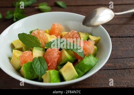 Salade végétarienne saine avec avocat, pamplemousse et feuilles de menthe dans un bol blanc sur une table en bois sombre Banque D'Images