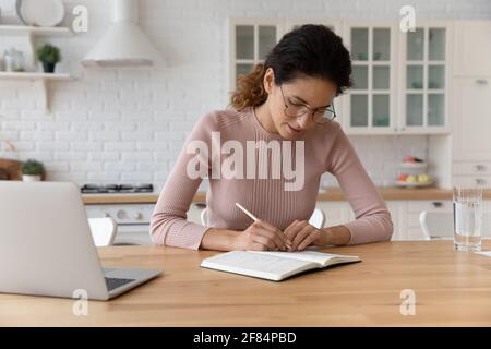 Une femme latine millénaire concentrée travaille avec un carnet papier pour faire des enregistrements Banque D'Images