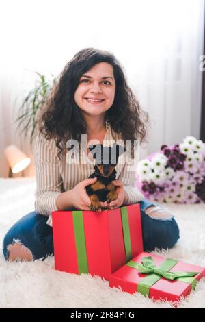 La jeune femme heureuse sort de la boîte cadeau mignon petit chiot. Broche miniature noire et Havane dans la main des femelles Banque D'Images