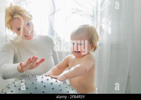 Maman est engagée dans la gymnastique avec le bébé sur un ballon gonflable. Fitball, gymnastique pour un enfant. Banque D'Images