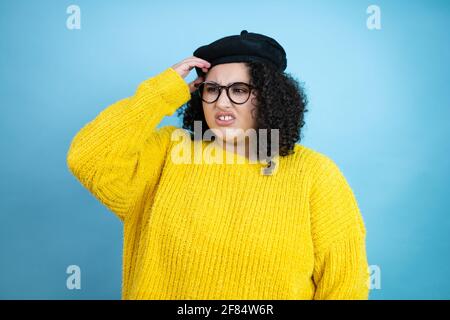 Jeune belle femme portant un look français avec béret et jaune chandail décontracté sur fond bleu isolé confusion et s'interroger sur la question. Non certif Banque D'Images