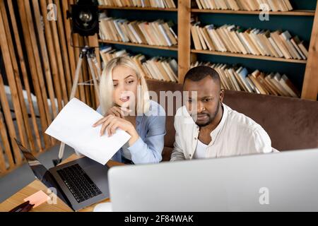 Collègues concentrés assis à la table, en utilisant l'ordinateur, en recherchant des idées pour le projet. Les partenaires d'affaires multiraciaux travaillent ensemble dans Banque D'Images