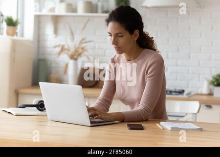 Femme millénaire latina travailler en ligne en utilisant un ordinateur portable à la cuisine à la maison Banque D'Images