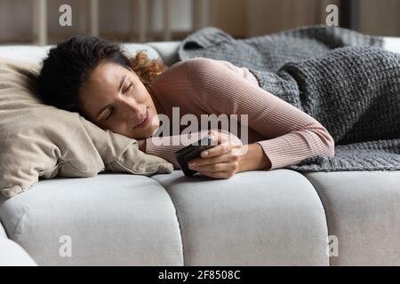 Une femme millénaire détendue se trouve sur le canapé et lit le message sur le smartphone Banque D'Images