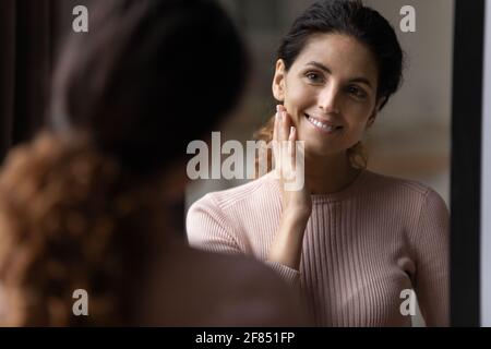 Femme hispanique millénaire regarder le miroir profiter d'une peau fraîche et saine Banque D'Images