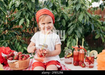 Lemonade Stand. Adorable petite fille essayant de vendre de la limonade. avec de la glace limonade aux fraises et à la menthe d'été comme boisson rafraîchissante dans les pots. Cold soft drin Banque D'Images