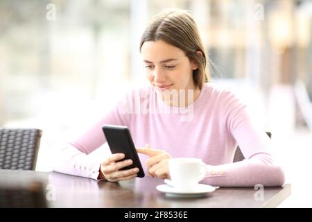 Femme satisfaite utilisant un smartphone assis dans un café une journée ensoleillée Banque D'Images