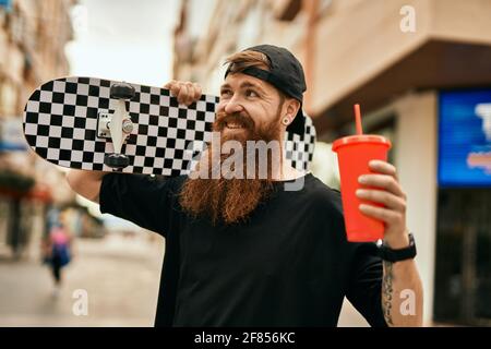 Jeune patineur irlandais tenant du skate et buvant du soda à la ville. Banque D'Images