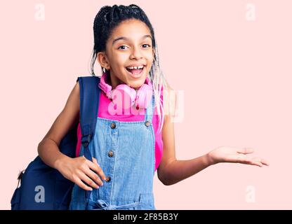 Adorable fille afro-américaine tenant un sac à dos étudiant en utilisant un sac à dos célébrant victoire avec un sourire heureux et une expression gagnante avec des mains levées Banque D'Images