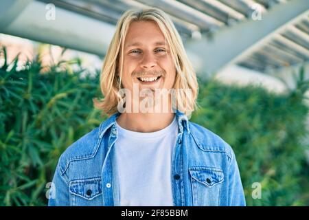 Jeune homme scandinave blond souriant heureux debout à la ville. Banque D'Images