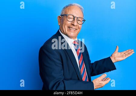 Homme caucasien senior portant un costume d'affaires et cravate invitant à entrez dans le sourire naturel avec la main ouverte Banque D'Images