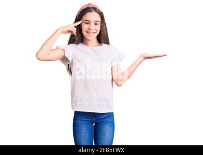 Adorable enfant hispanique fille portant un chandail blanc décontracté confus et ennuyé avec la paume ouverte montrant l'espace de copie et le doigt pointant vers le front. Pensez abo Banque D'Images