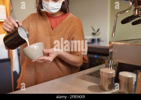 Dose de barista féminin en train de préparer du latte avec de la crème tout en faisant du café frais dans un café ou un café, dans un espace de copie Banque D'Images