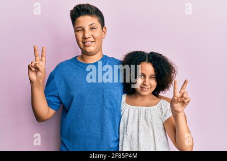 Jeune famille hispanique de frère et de soeur portant des vêtements décontractés ensemble, souriant et visage souriant se faisant à l'appareil photo signe de victoire avec le surf Banque D'Images