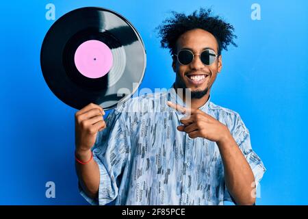 Jeune africain américain avec la barbe tenant un disque en vinyle souriant contenchez-vous de pointer avec votre main et votre doigt Banque D'Images