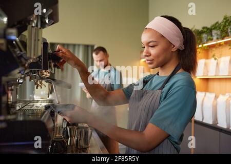 Portrait de la jeune femme Barista en vue latérale pour préparer un café frais dans le café et la machine à café en fonctionnement Banque D'Images