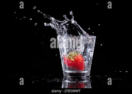 photo en studio de fraises et de glace déposées dans un verre d'eau sur fond noir. Banque D'Images