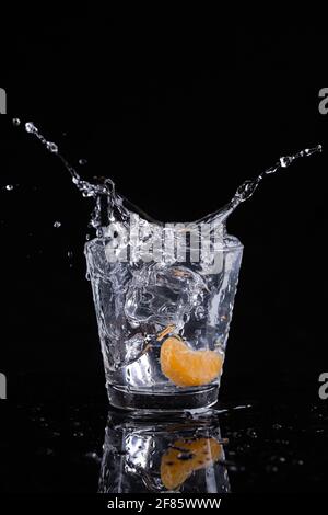 Une photo en studio de glaçons déposés dans un verre d'eau avec une tranche d'orange. Banque D'Images