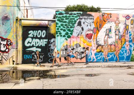 Une famille de touristes se promène dans une rue avec des œuvres d'art couvrant chaque mur en vue dans le quartier artistique de Wynwood, Miami, Floride, États-Unis Banque D'Images