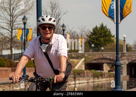 Frederick, MD, États-Unis 04-07-2021: Un homme caucasien âgé fait du vélo seul lors d'une journée ensoleillée dans le parc de Carroll Creek. Il porte un t-shirt et un casque décontractés. A h Banque D'Images