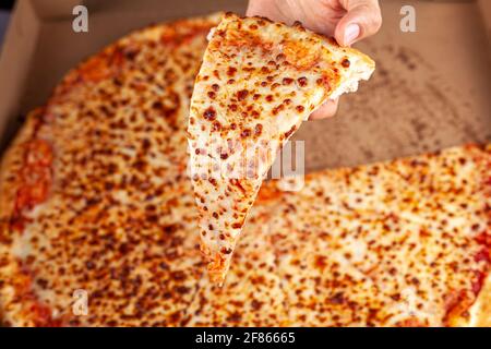 Gros plan vue du dessus d'une femme caucasienne tenant une tranche de pizza au fromage frais avec une grande pizza dans une boîte à carboard en arrière-plan. Image de concept pour Banque D'Images