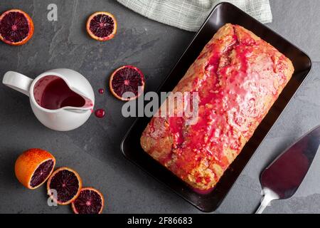 Image en gros plan d'un gâteau d'orange de sang frais fait maison dans un moule à pain et servi sur une assiette en porcelaine noire sur fond de pierre sombre. Il a l'orang de sang Banque D'Images