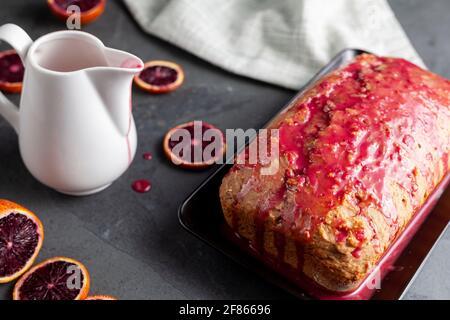 Image en gros plan d'un gâteau d'orange de sang frais fait maison dans un moule à pain et servi sur une assiette en porcelaine noire sur fond de pierre sombre. Il a l'orang de sang Banque D'Images