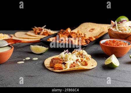 Image en gros plan d'un plat mexicain de tacos avec des tortillas de maïs, morceaux de poulet précuits, précuits, limaces de chou, fromage râpé, sauce salsa et crème Banque D'Images