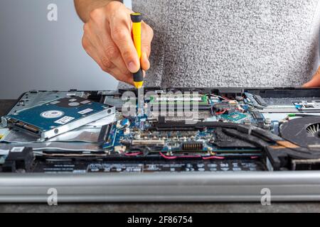 Un technicien en informatique répare un ancien ordinateur portable à l'aide d'un tournevis. Image isolée en gros plan montrant l'intérieur complexe d'un ordinateur portable avec cartes de circuit imprimé Banque D'Images