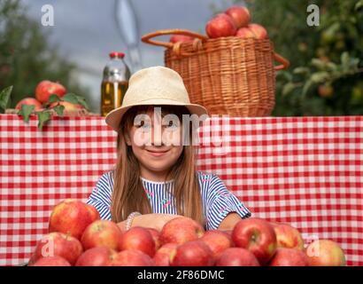 Portrait de petite fille souriante avec de beaux yeux dans un verger. Concept d'alimentation saine. Mignonne fille et Arrangement d'automne avec pommes et jus de pomme. Banque D'Images