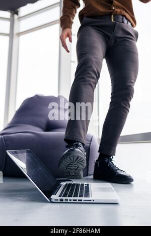 Un pied d'homme à chaussures se trouve à proximité de l'ordinateur portable. L'homme veut monter sur son ordinateur portable Banque D'Images