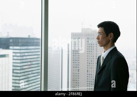 Homme d'affaires avec vue sur la grande fenêtre de bureau urbaine Banque D'Images