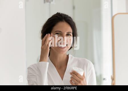 Portrait de tête de prise de vue femme surjoyeuse appliquant une lotion hydratante sur la joue Banque D'Images