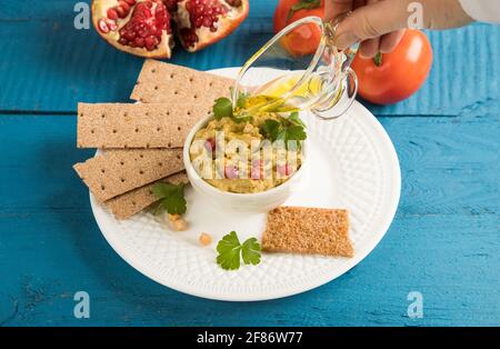 La main d'une femme verse de l'huile d'olive dans un en-cas hummus de pois turcs. Banque D'Images